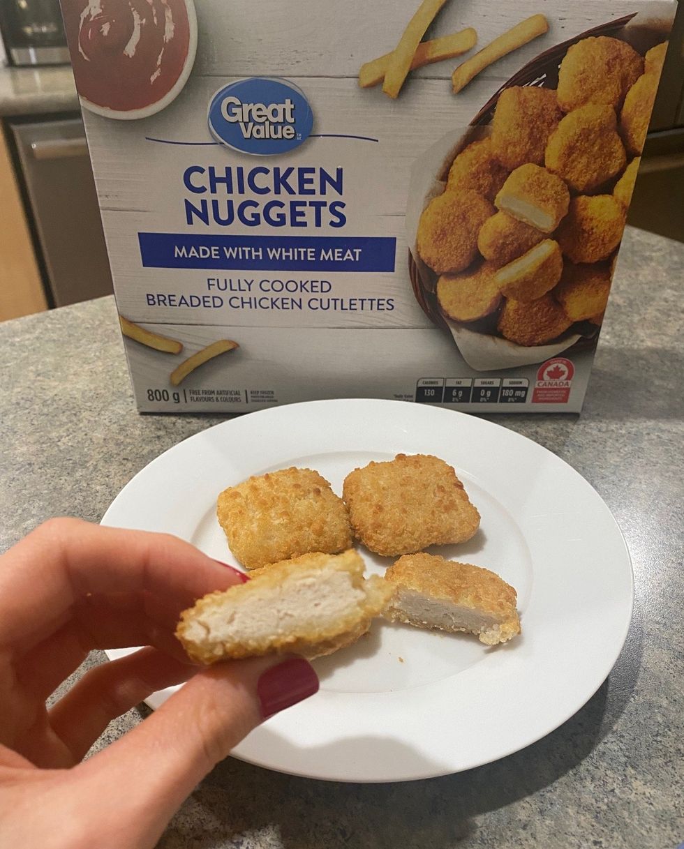 Asymina holding a piece of a Great Value chicken nugget above a plate of nuggets.
