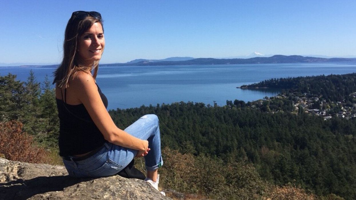 Asymina sitting on a rock and smiling at the camera, with a backdrop of Victoria, BC.