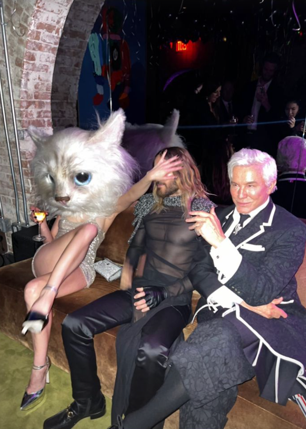 Aubrey Plaza wearing a cat costume head and sitting next Jared Leto.