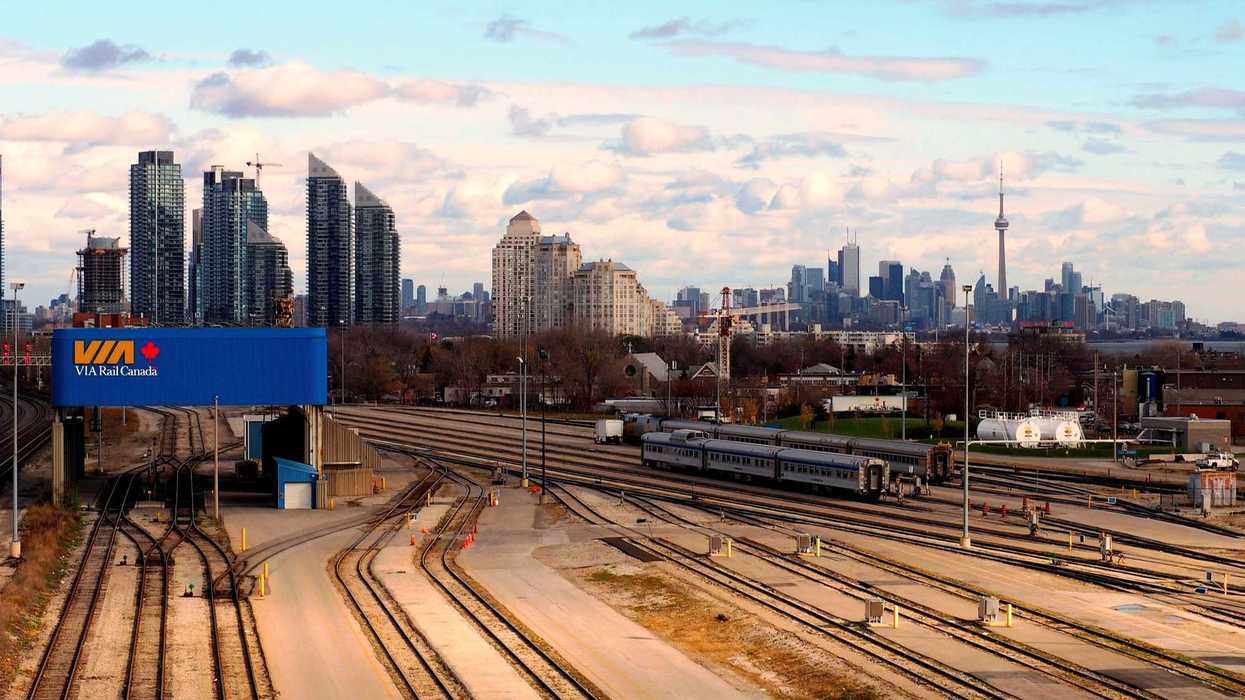 blue via rail sign above train tracks with toronto skyline in background