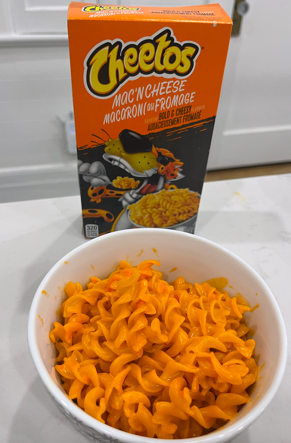 Bo\u00eete de macaronis au fromage de marque Cheetos et son bol de macaronis pr\u00e9par\u00e9s, de couleur orange fluo.
