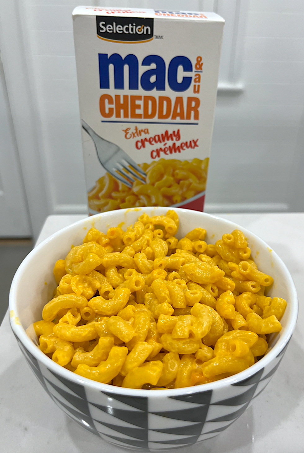 Bo\u00eete de macaronis au fromage de marque S\u00e9lection et un bol de macaronis pr\u00e9par\u00e9s.