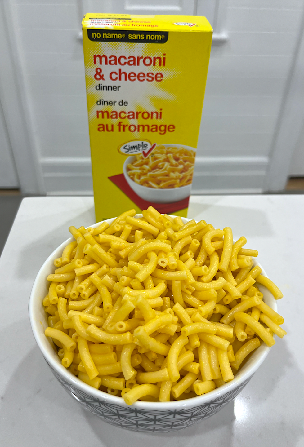 Bo\u00eete de macaronis au fromage de marque Sans Nom et un bol de macaronis pr\u00e9par\u00e9s.