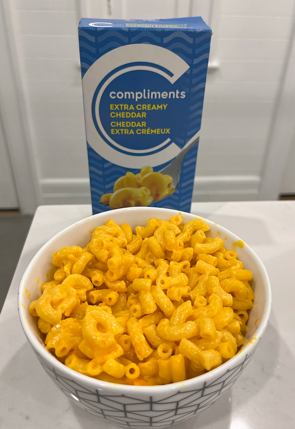 Bo\u00eete de macaronis au fromage de marque \u200bCompliments et un bol de macaronis pr\u00e9par\u00e9s.
