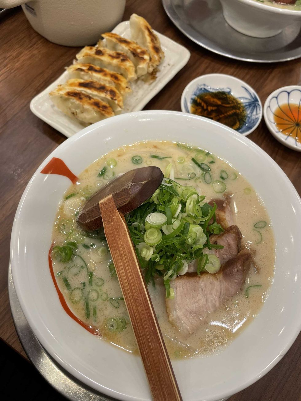 Bowl of ramen topped with green onions, with gyoza dumplings in the background.