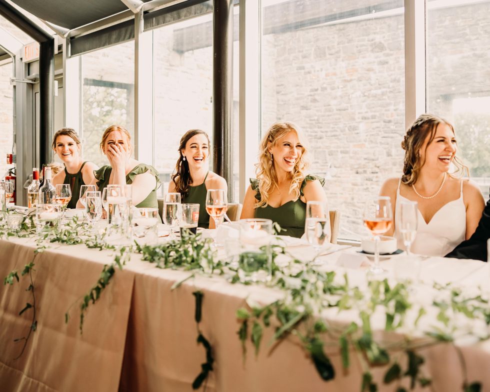 Bride and bridesmaids at dinner, laughing during a wedding speech.