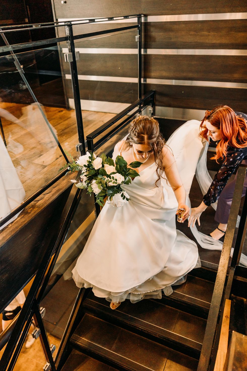 Brittany Frid helps the bride down the stairs with her bouquet and a shot of whiskey.