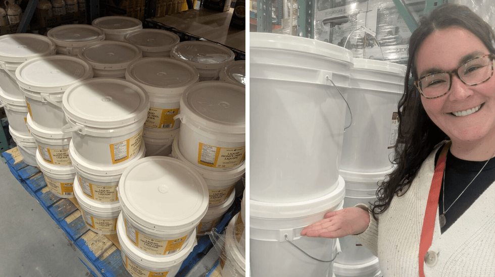 Buckets of honey stacked in store; a woman smiling and gesturing at them.