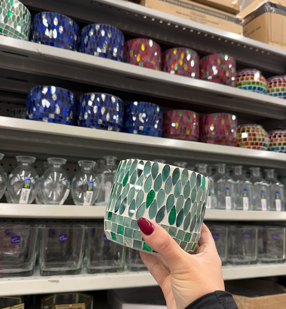 Cache-pot d\u00e9coratif en mosa\u00efque verte tenu \u00e0 la main dans une all\u00e9e Dollarama, avec d\u2019autres couleurs visibles en arri\u00e8re-plan.