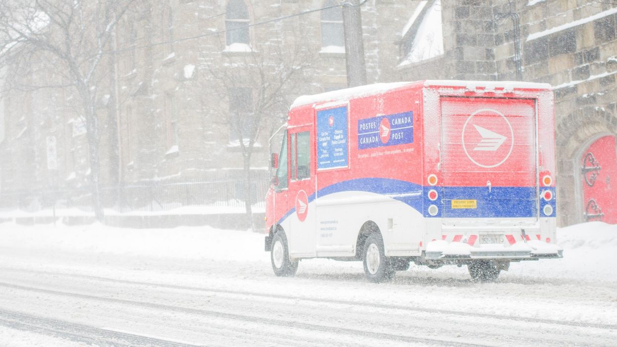 Canada Post delivery truck driving down a street in a snowstorm.