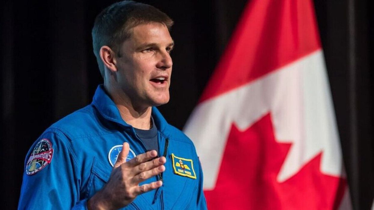 Canadian astronaut Jeremy Hansen speaking in front of a Canadian flag.