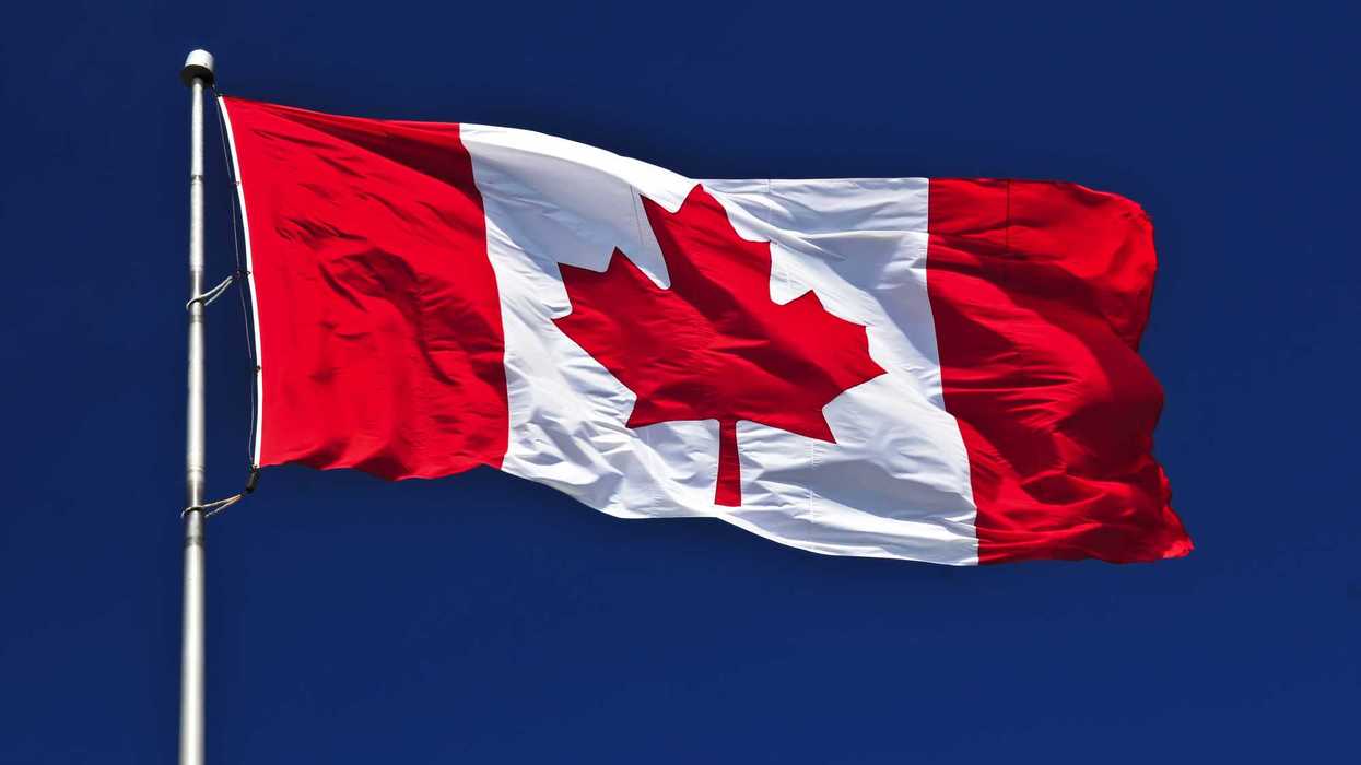 Canadian flag waves against a blue sky.