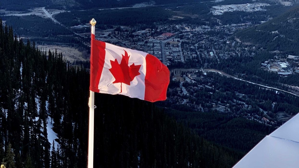 canadian flag with snow covered mountains and trees behind it