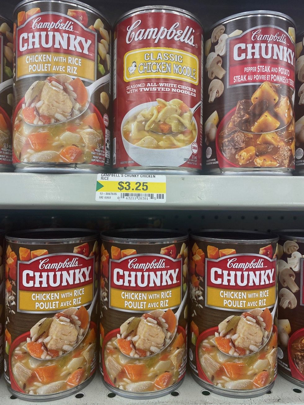 Cans of soup in a store that say Campbell's Chunky on the label and have various flavours like chicken and rice.