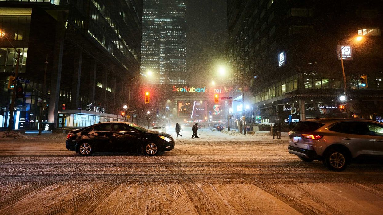 cars and people on a toronto street while it snows