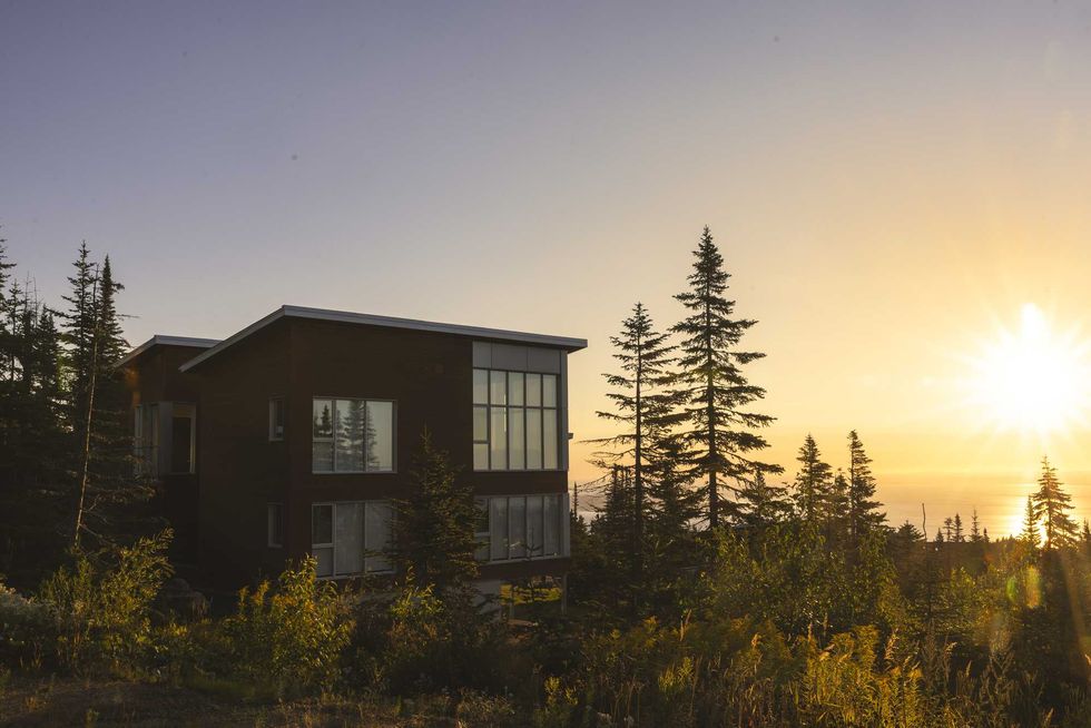 Chalet contemporain entour\u00e9 de conif\u00e8res au coucher du soleil avec vue sur le paysage forestier.