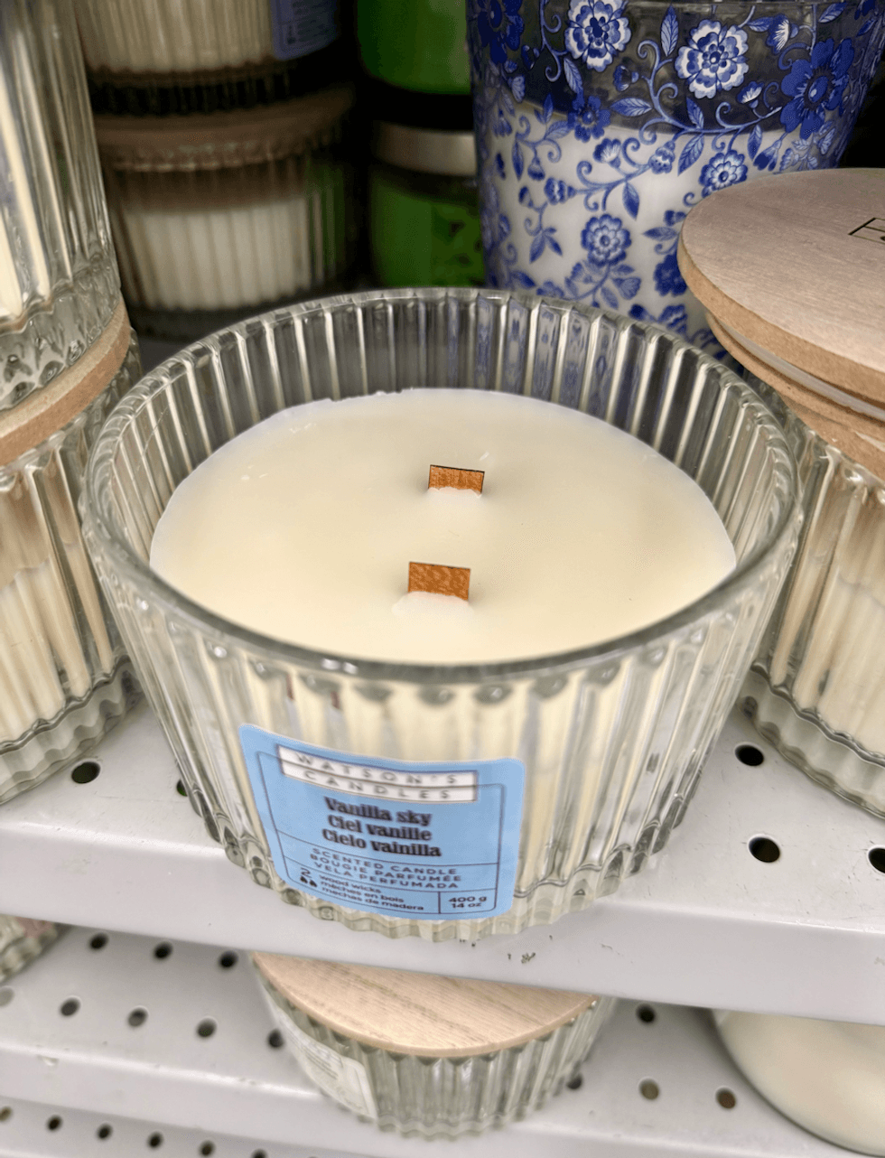 Chandelle parfum\u00e9e \u00e0 deux m\u00e8ches dans un pot en verre textur\u00e9 avec couvercle en bois, sur une \u00e9tag\u00e8re chez Dollarama.