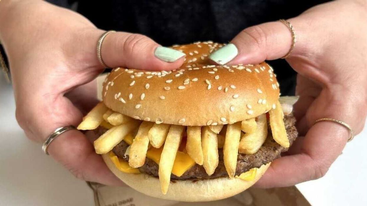 Cheeseburger au steak, fromage et frites dans un pain brioché aux graines de sésame, tenu à deux mains.