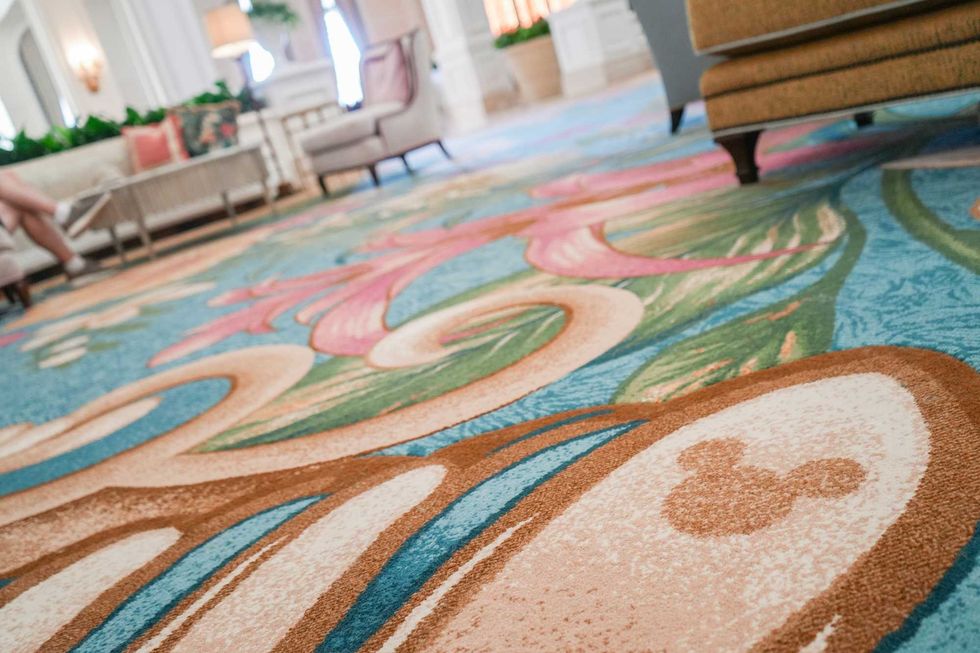 Close-up of the Grand Floridian lobby carpet with a floral pattern in pink, blue and green, with a subtle Mickey Mouse silhouette woven into the design.