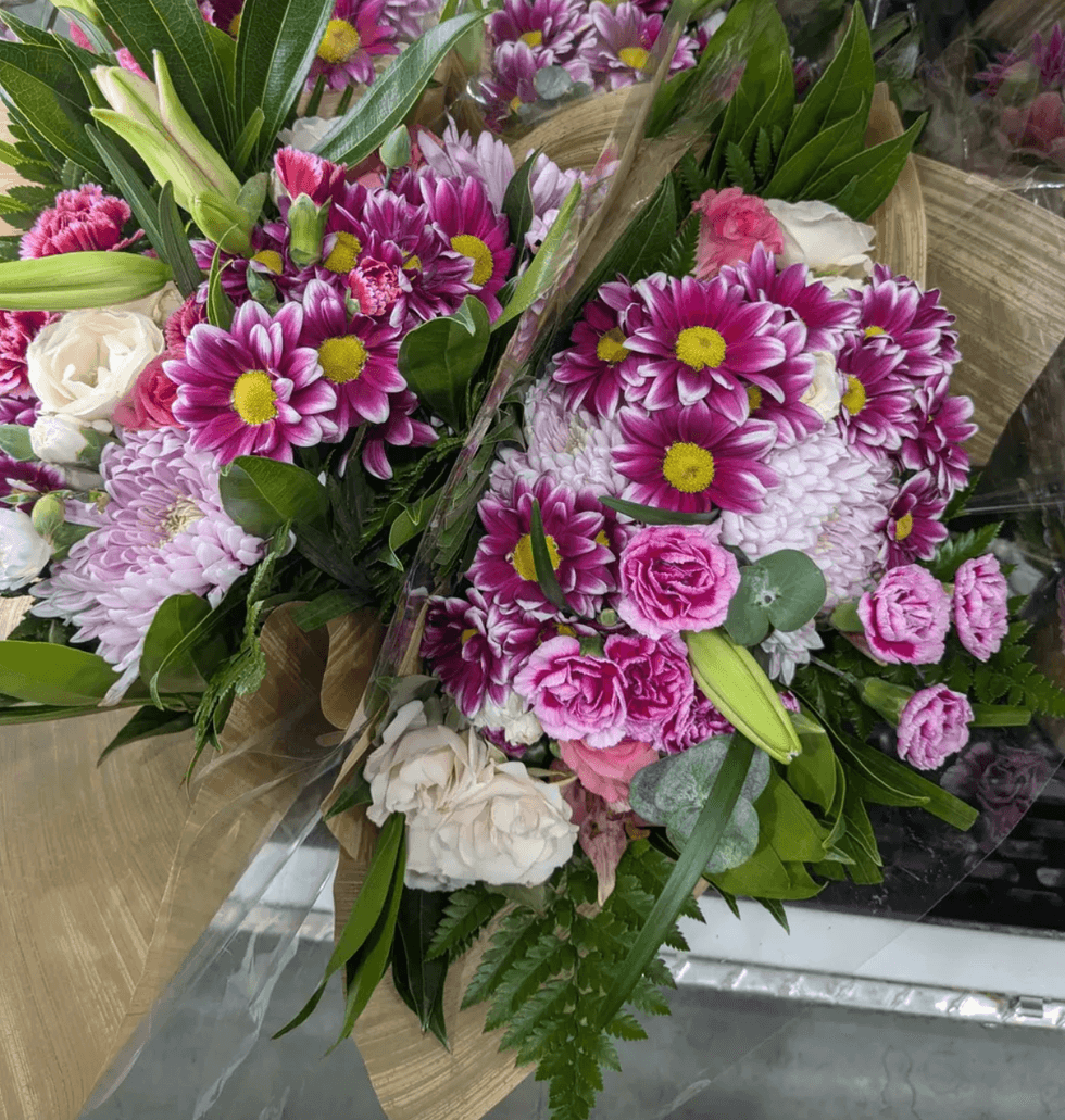 Colorful bouquet with pink daisies, roses, and lush green leaves.