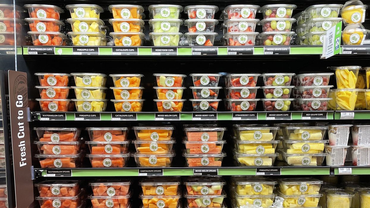 Containers of fresh cut fruit in clear plastic stacked in an open fridge.