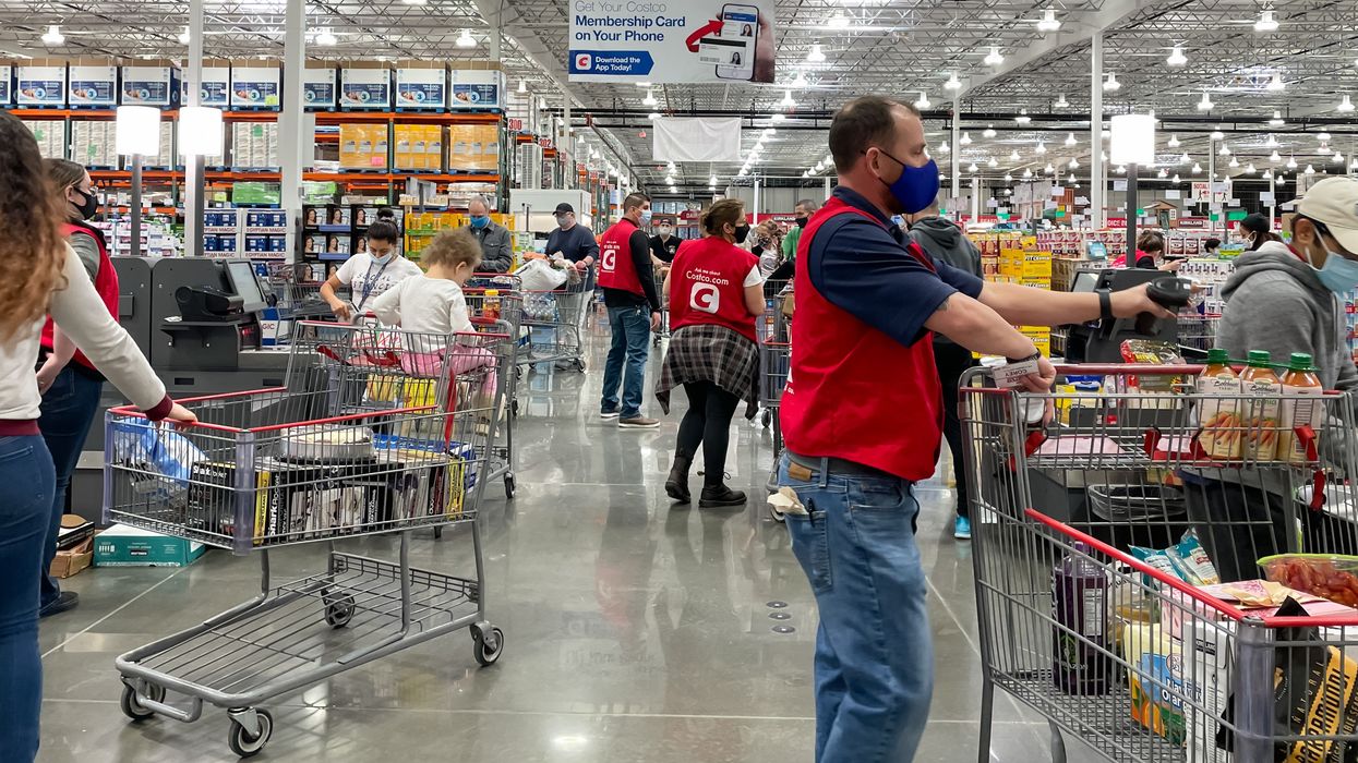 costco employees in red vests helping shoppers at the self-checkout lanes in a warehouse