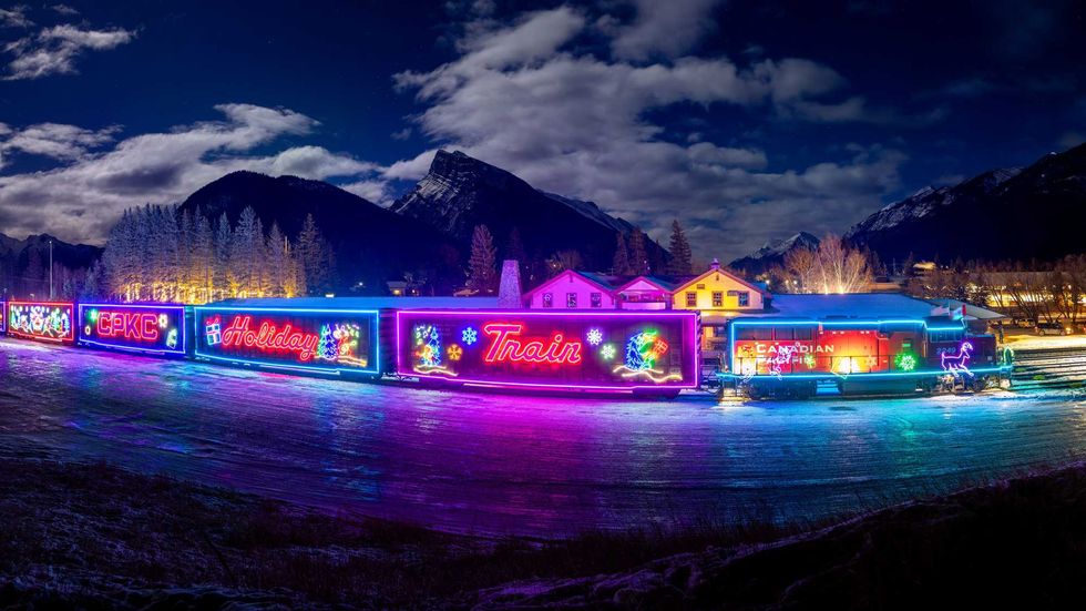cpkc holiday train lit up at night with mountains in the background