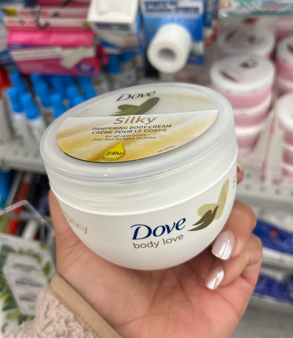 Cr\u00e8me pour le corps \u00ab Silky \u00bb de Dove dans une main.