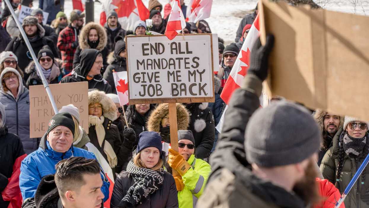 Crowd of protesters, one holding a sign reading "end all mandates give me my job back."