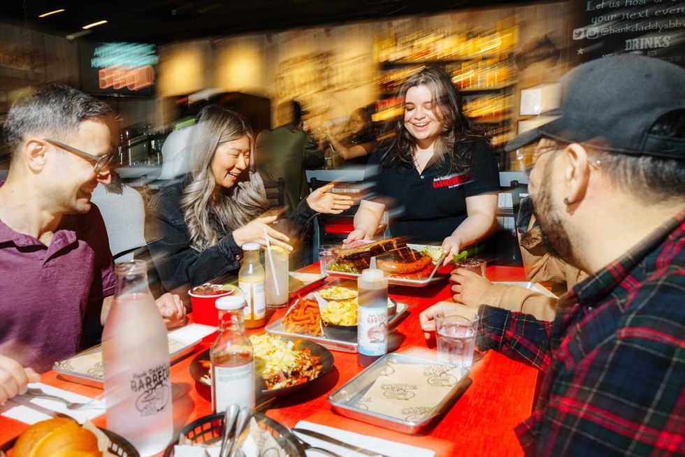 Customers sit around a table at Hank Daddy's as a smoked meat platter is delivered to the table.