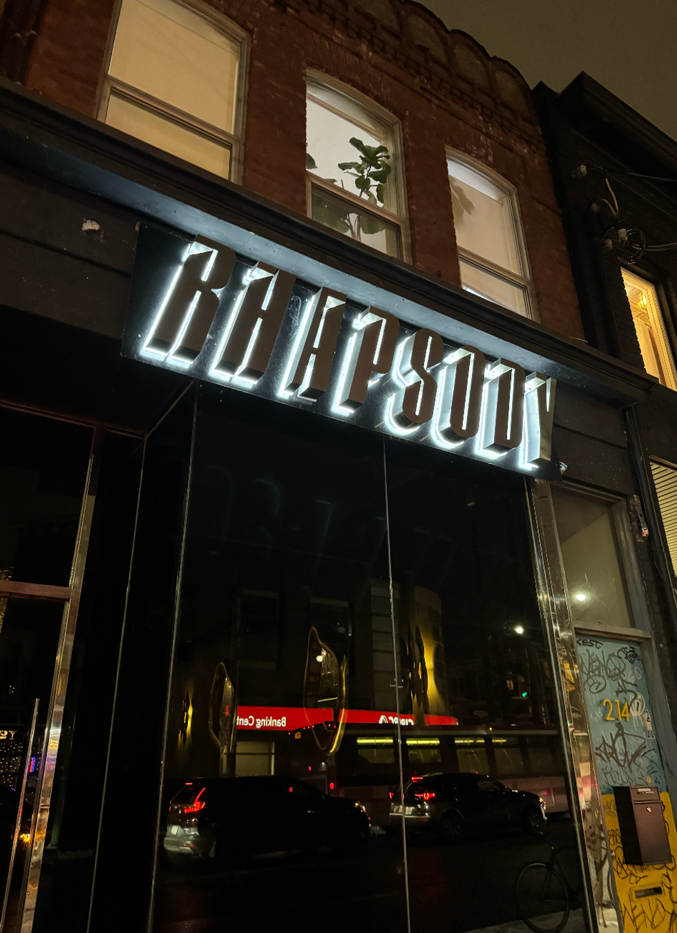 Dark, glassy doors beneath a lit-up sign reading "Rhapsody."