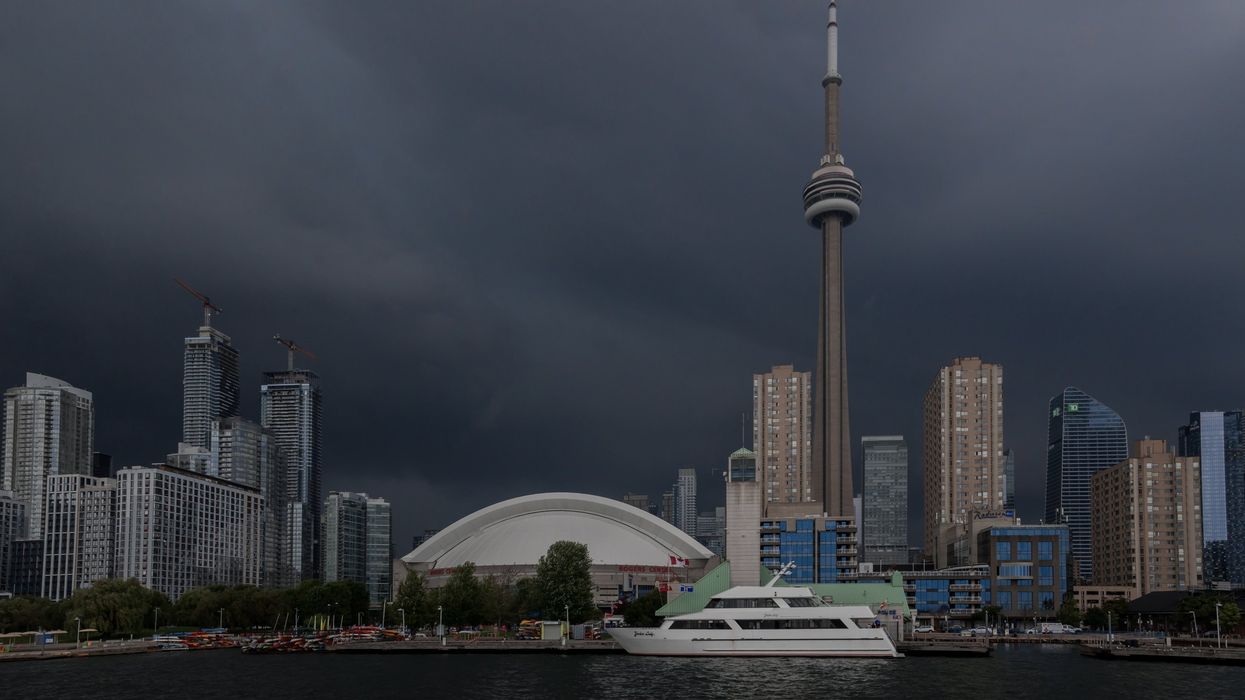 Dark skies before a storm in Toronto with a yacht in Lake Ontario and Rogers Centre and the CN Tower in the background.