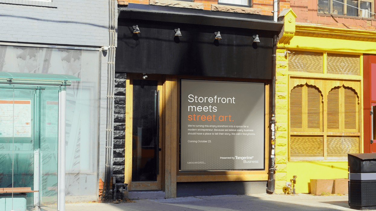 Dark storefront with a Tangerine Business “Storefront meets street art” sign between two buildings.