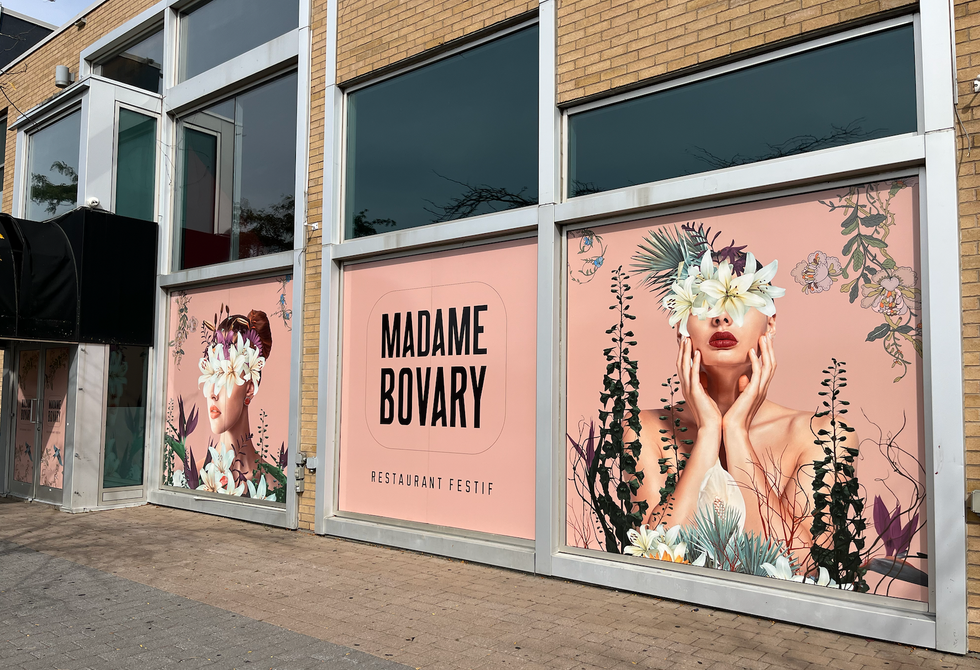 Des affiches tapissant les fen\u00eatres d'une b\u00e2tisse pr\u00e9sentant le restaurant festif Madame Bovary.