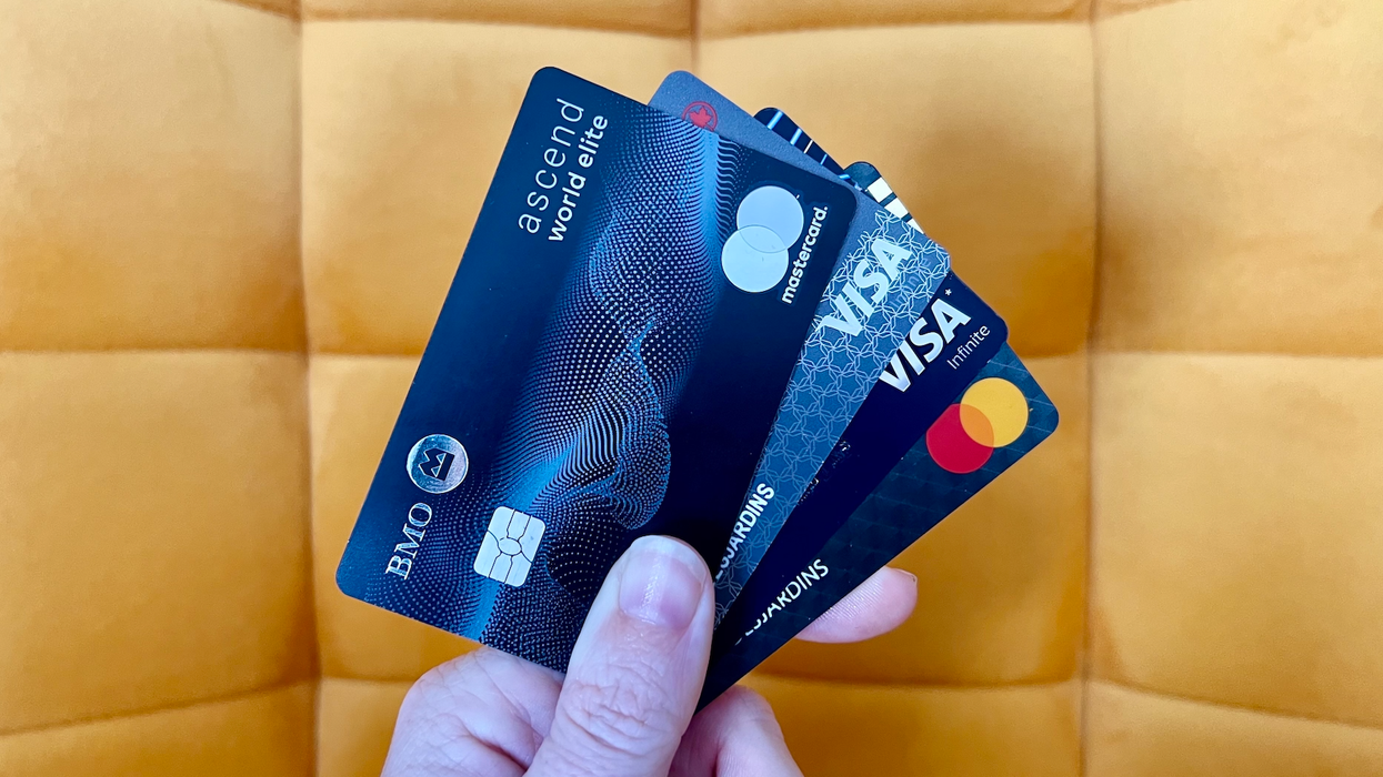 Des cartes de crédit placées en éventail dans une main devant une chaise jaune.