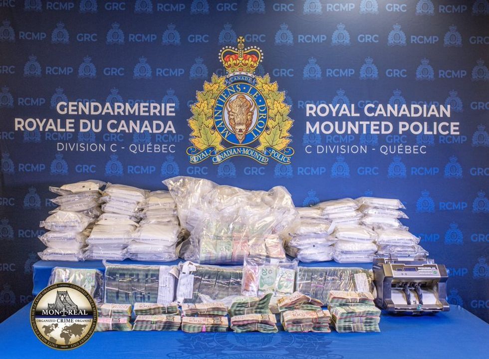 Des centaines de billets de banque ainsi que des sacs remplis de coca\u00efne sont \u00e9tal\u00e9s sur une table bleu avec le logo de la GRC.