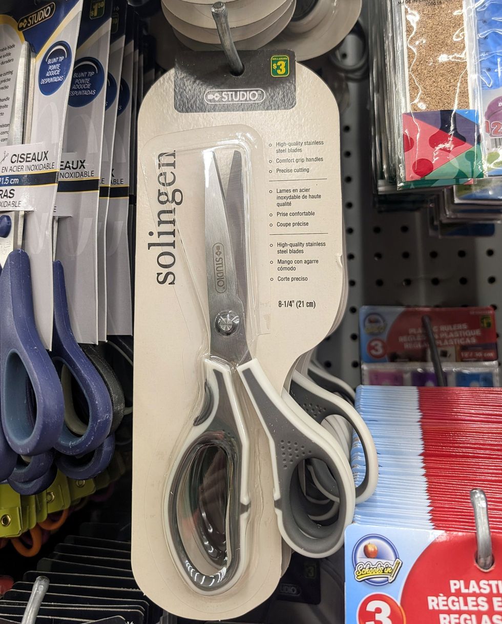 Des ciseaux gris et blanc vendus dans la rang\u00e9e des fournitures scolaires chez Dollarama.