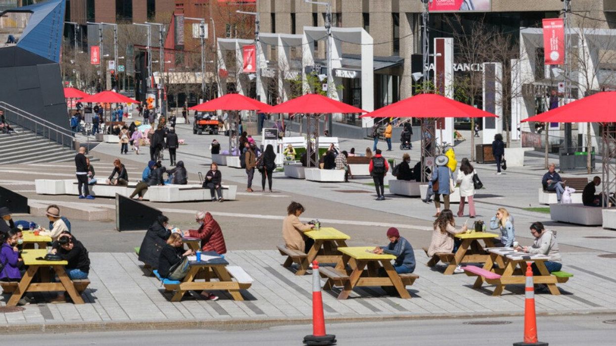 Des gens assis à des tables de pique-nique dans le centre-ville de Montréal.
