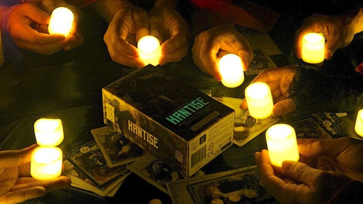 Des mains tenant des chandelles devant le jeu de société immersif Hantise.