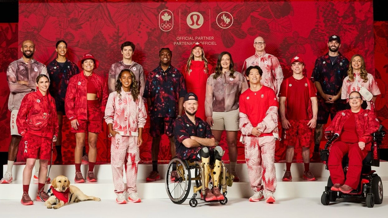 Des membres de la délégation canadienne en rouge et blanc ainsi qu'un chien posent devant un mur rouge.