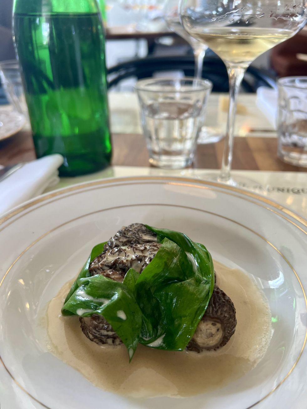 Des morilles farcies \u00e0 la cr\u00e8me avec de la verdure dans une assiette blanche et dor\u00e9e.