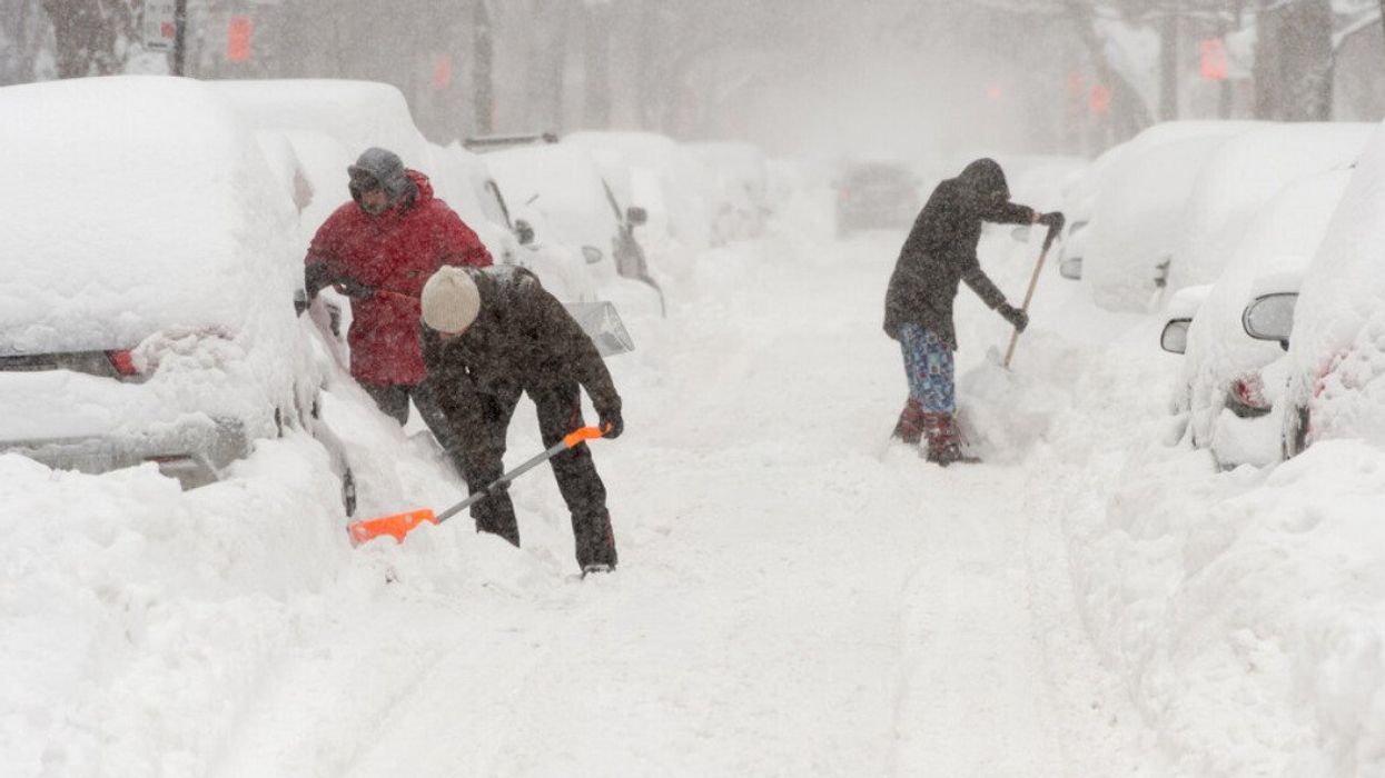 Des personnes pellètent la neige autour de leur véhicule dans une rue enneigée à Montréal.