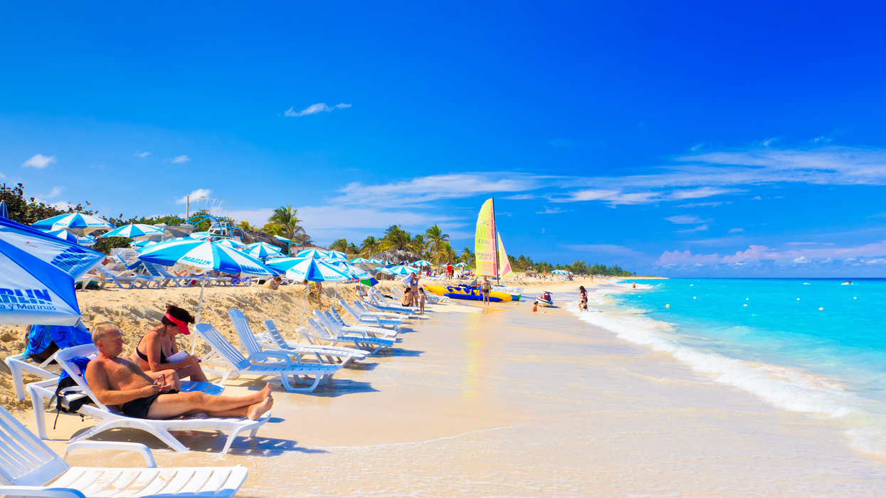 Des personnes se prélassent sur des chaises longues blanches devant une mer turquoise à Cuba.