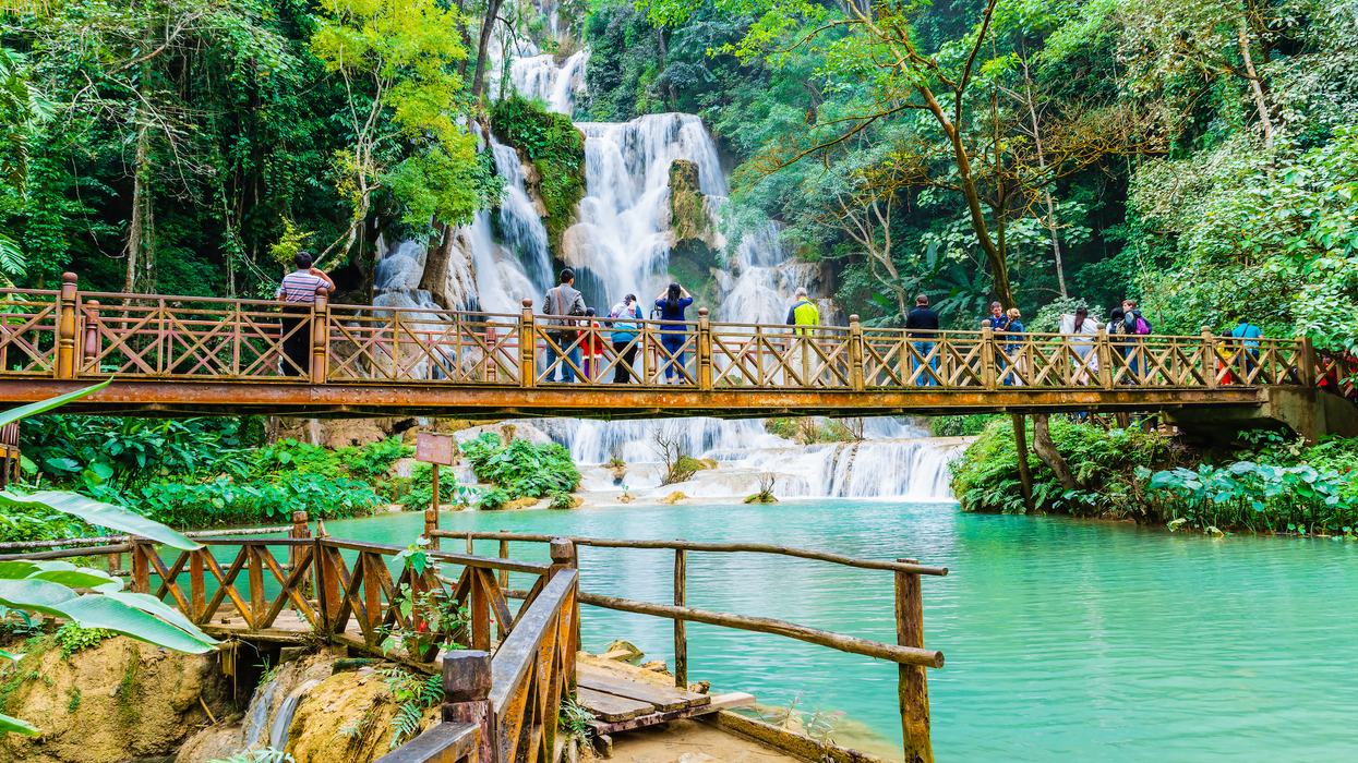 Des personnes se promènent sur une passerelle et prennent en photo une immense chute d'eau au Laos.