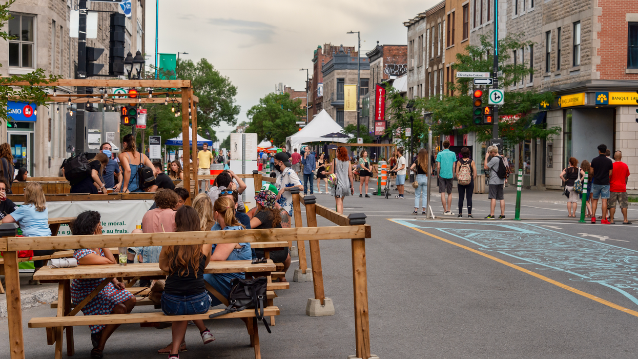 Des personnes sont assises sur des tables à pique-nique aux abords d'une rue piétonne à Montréal.