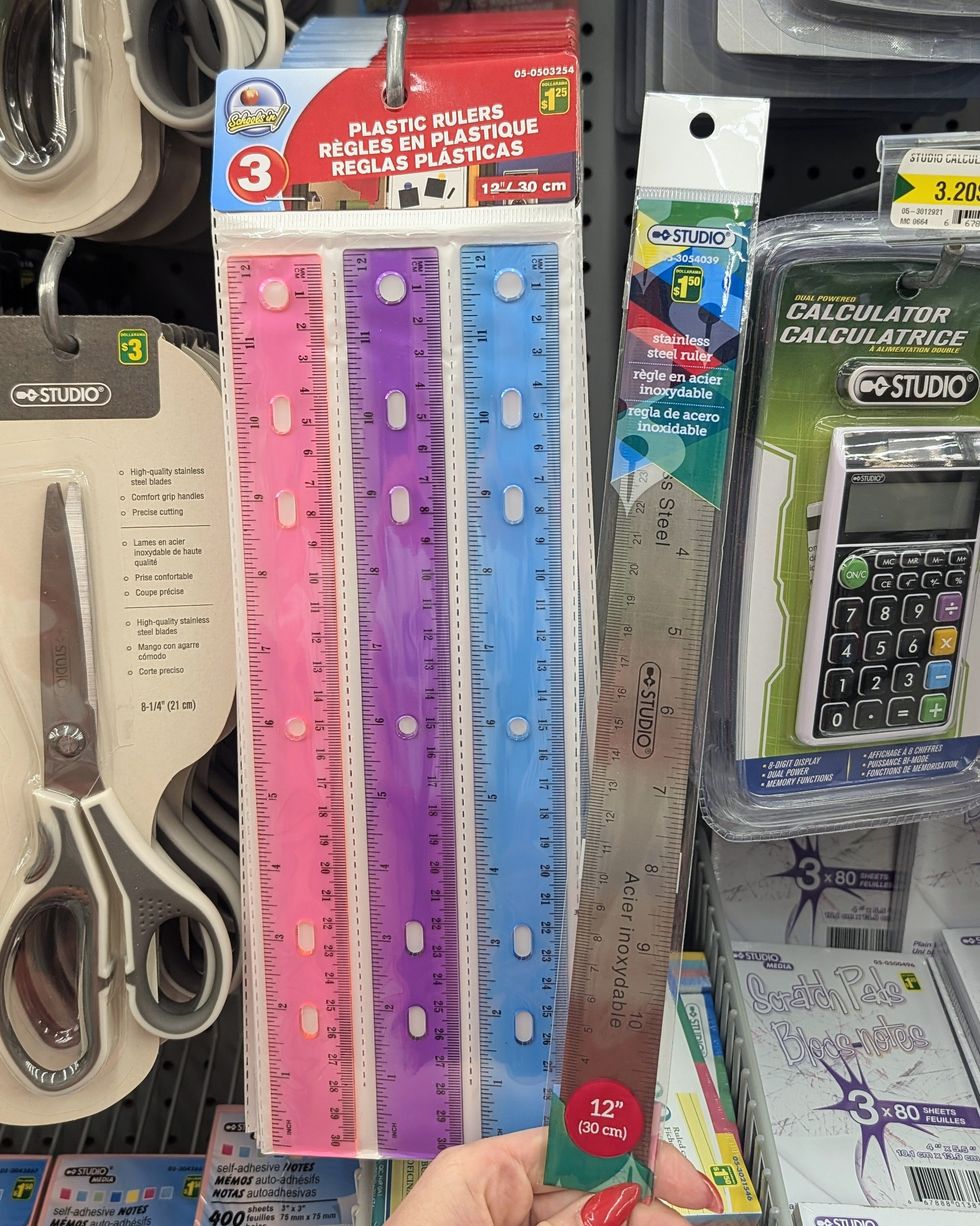 Des r\u00e8gles color\u00e9es en plastique et une r\u00e8gle en m\u00e9tal et li\u00e8ge vendues dans la rang\u00e9e des fournitures scolaires chez Dollarama.