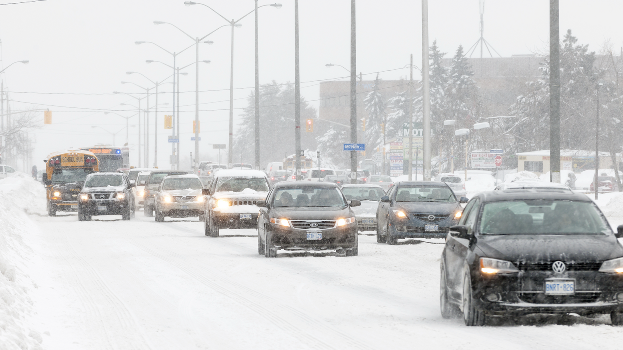 Des véhicules se déplacent sur une route enneigée avec des flocons qui tombent.