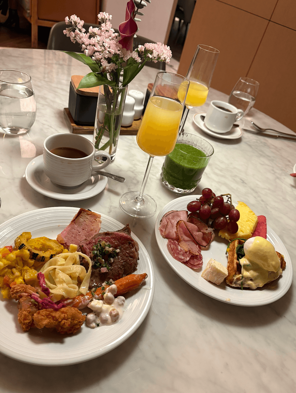 Deux assiettes garnies de plats chauds et froids du brunch \u00e0 volont\u00e9 du restaurant Lloyd, accompagn\u00e9es de mimosas, de caf\u00e9 et d'un jus vert.