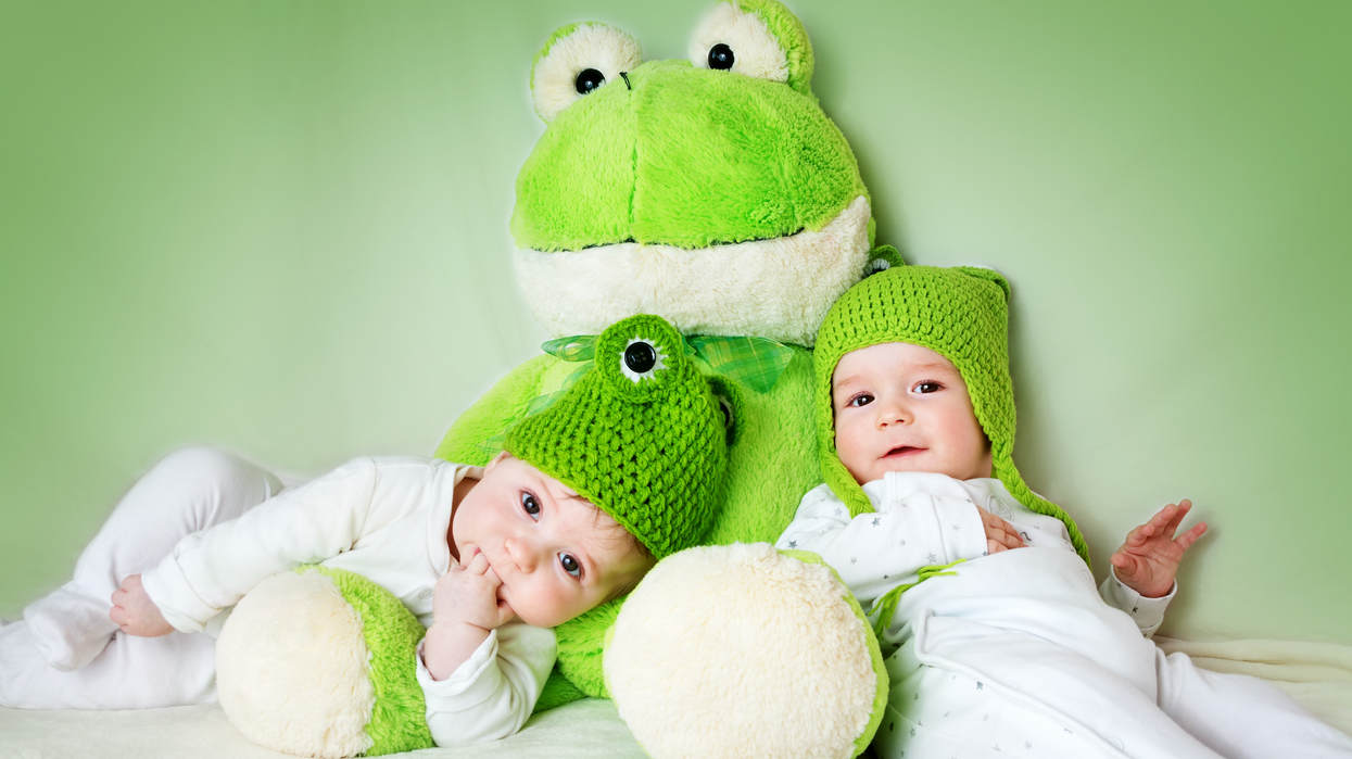 Deux bébés avec des tuques vertes prennent la pose sur un toutou en forme de grenouille.