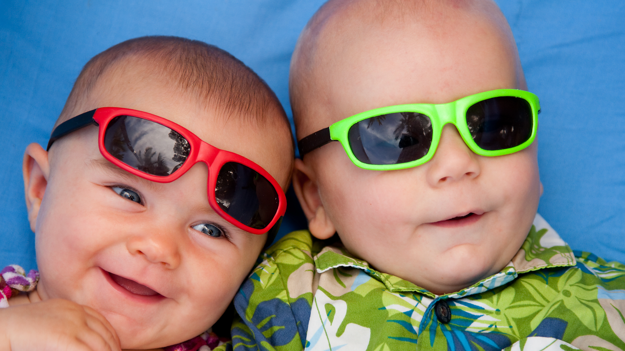 Deux bébés côte-à-côte sourient avec des lunettes de soleil colorées.